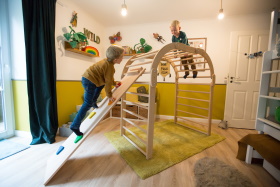 Kinder spielen im Zimmer mit einem hohen Kletterbogen und einem angelehnten Kletterbrett mit bunten Griffen.
