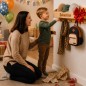 Preview: Weihnachtsszene mit Mutter und Kind, die sich über eine personalisierte Garderobe freuen; Produkt hängt an der Wand, Gravur gut lesbar, Weihnachtsbaum daneben.
