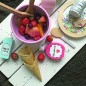 Preview: Serviervorschlag für das Fruchtsalat-Set JB-W7161: Rosa Schüssel mit Spielzeug-Früchten, Eiswaffeln und Saucenflaschen auf einem weißen Holztisch