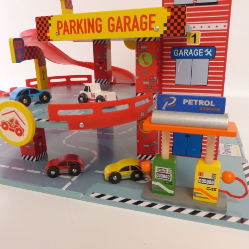 Spielzeug-Garage mit einem rot-weiß gestreiften Aufzugsschacht, einer Zapfsäule an der Seite und mehreren bunten Holzautos auf den Fahrbahnen