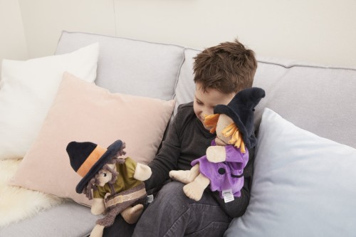Junge sitzt auf dem Sofa und denkt sich Rollenspiele mit der Räuber und Hexe Handpuppe aus