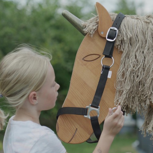 Kind legt dem Holzpferd Einhorn ein Halfter um