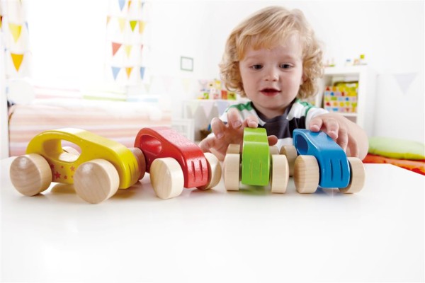 Kleinkind spielt mit bunten Holzautos.