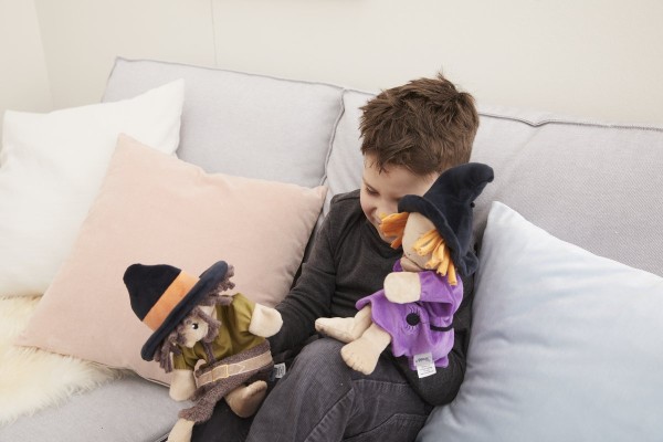 Junge sitzt auf dem Sofa und denkt sich Rollenspiele mit der Räuber und Hexe Handpuppe aus
