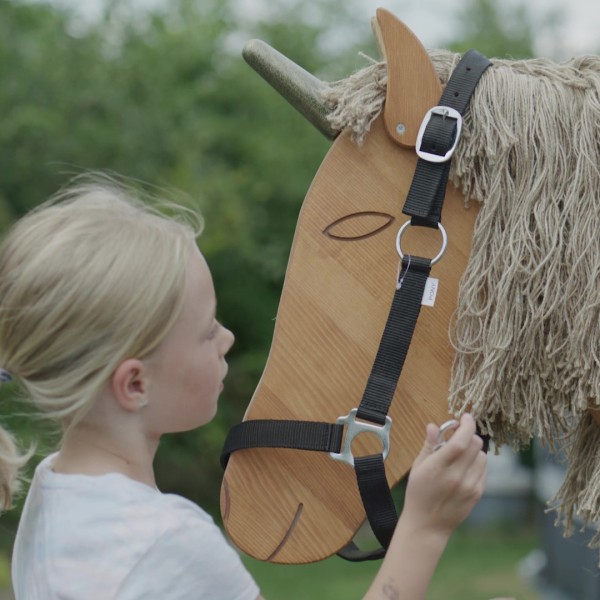 Kind legt dem Holzpferd Einhorn ein Halfter um